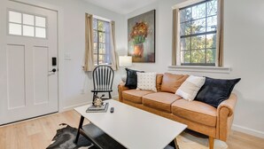 Ett vardagsrum med en beige soffa, ett vitt soffbord, en svart stol och en tavla på väggen.