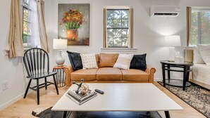Ett modernt vardagsrum med ett vitt soffbord, en brun lädersoffa, en svart stol och en tavla med blommor på väggen.