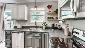 A modern kitchen with a built-in dishwasher, stainless steel appliances, and a window with a view of greenery. - Modern Retreat w/ Fire Pit Near Harrison Bay! (Chattanooga)