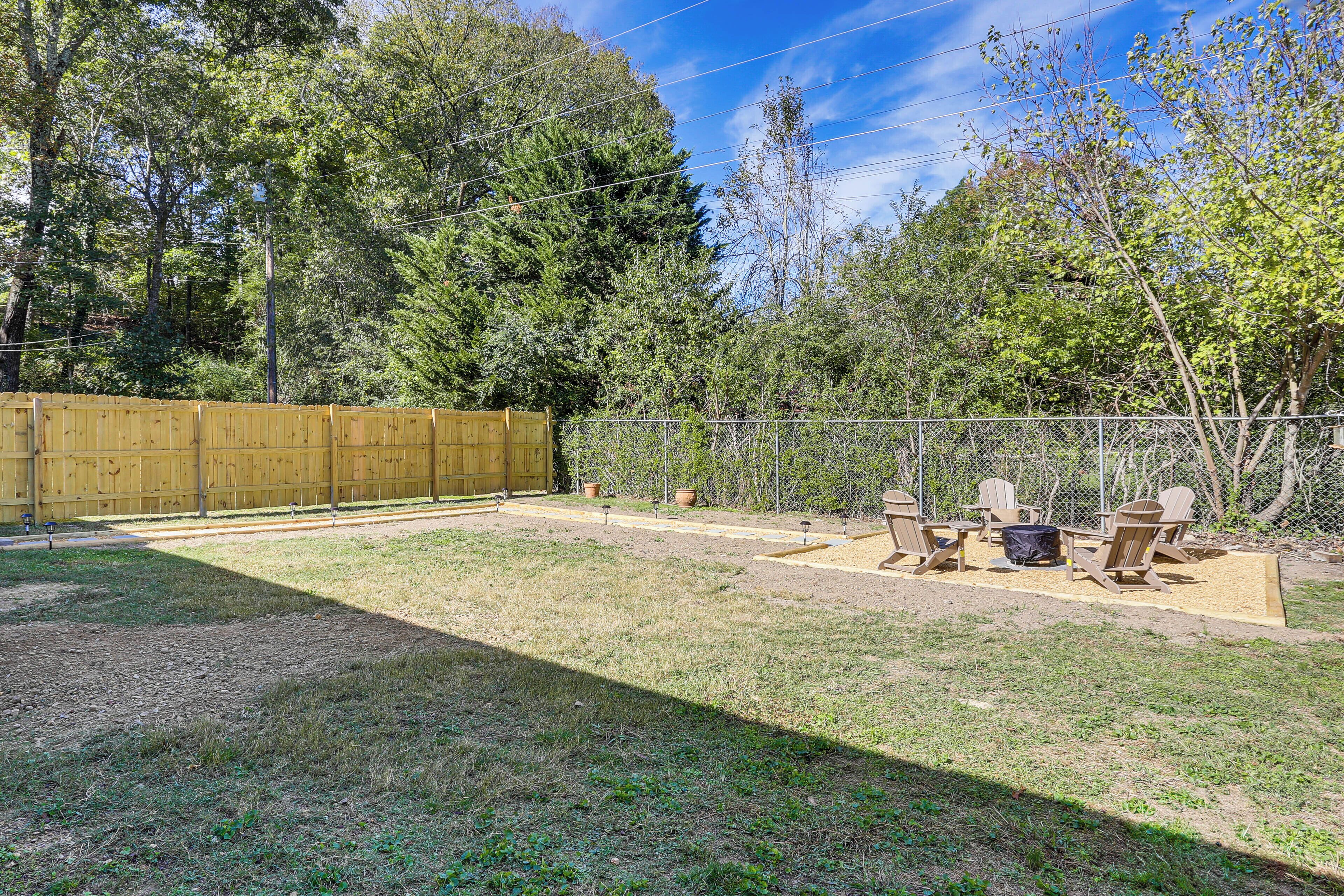 A fenced backyard with a grassy area, a wooden deck, and a seating arrangement with chairs and a table.