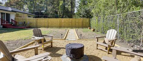 A backyard with Adirondack chairs, a fire pit, and a wooden fence.
