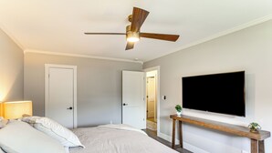 A bedroom with a bed, a ceiling fan, a TV mounted on the wall, and a door leading to another room. - Modern Retreat w/ Fire Pit Near Harrison Bay! (Chattanooga)