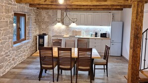 Une cuisine rustique avec des murs en pierre, des poutres en bois, une table à manger avec des chaises et des appareils électroménagers modernes.