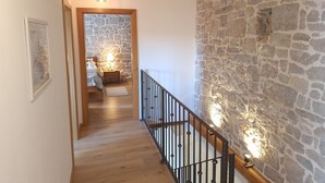 Un escalier en bois avec des murs en pierre, un lit avec une table de chevet et un luminaire suspendu.