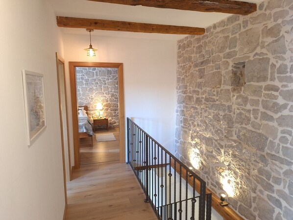 A wooden staircase with stone walls, a bed with a nightstand, and a hanging light fixture.