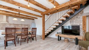 Une cuisine moderne avec des meubles blancs, un coin repas avec des chaises en bois, un escalier avec des marches en bois et un téléviseur à écran plat posé sur un meuble en bois.