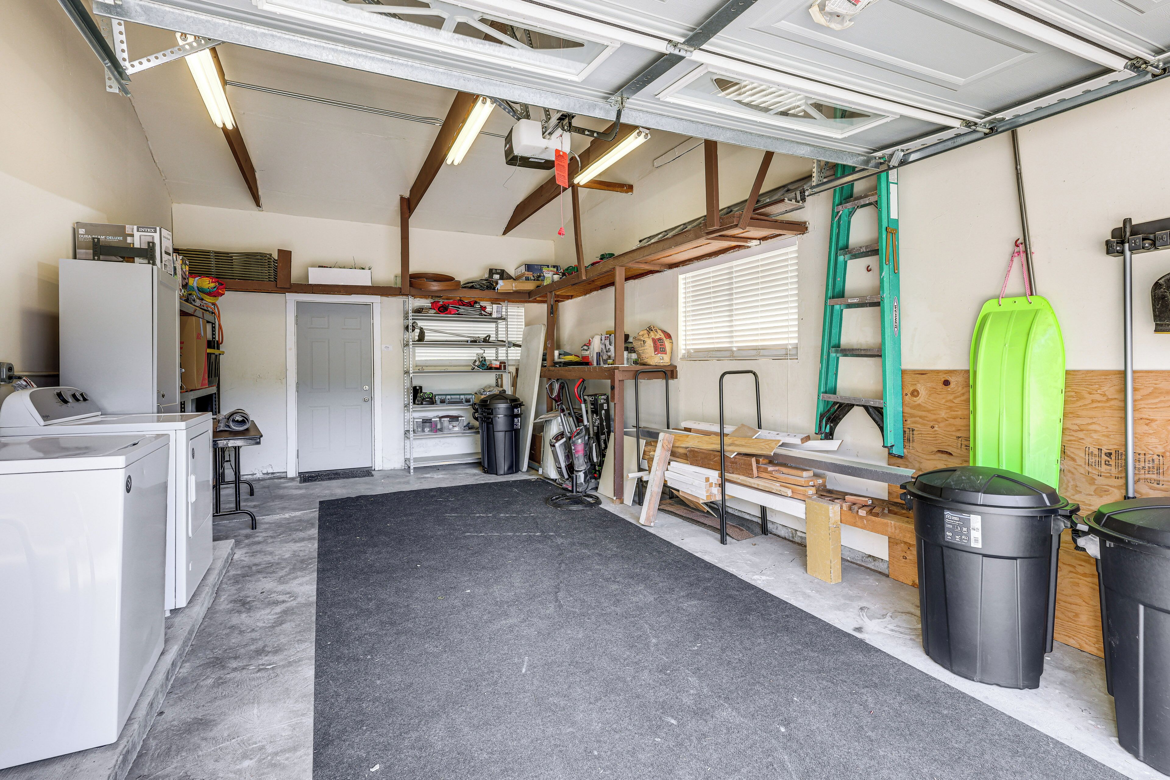 A garage with a workbench, storage shelves, a ladder, and a green bucket.