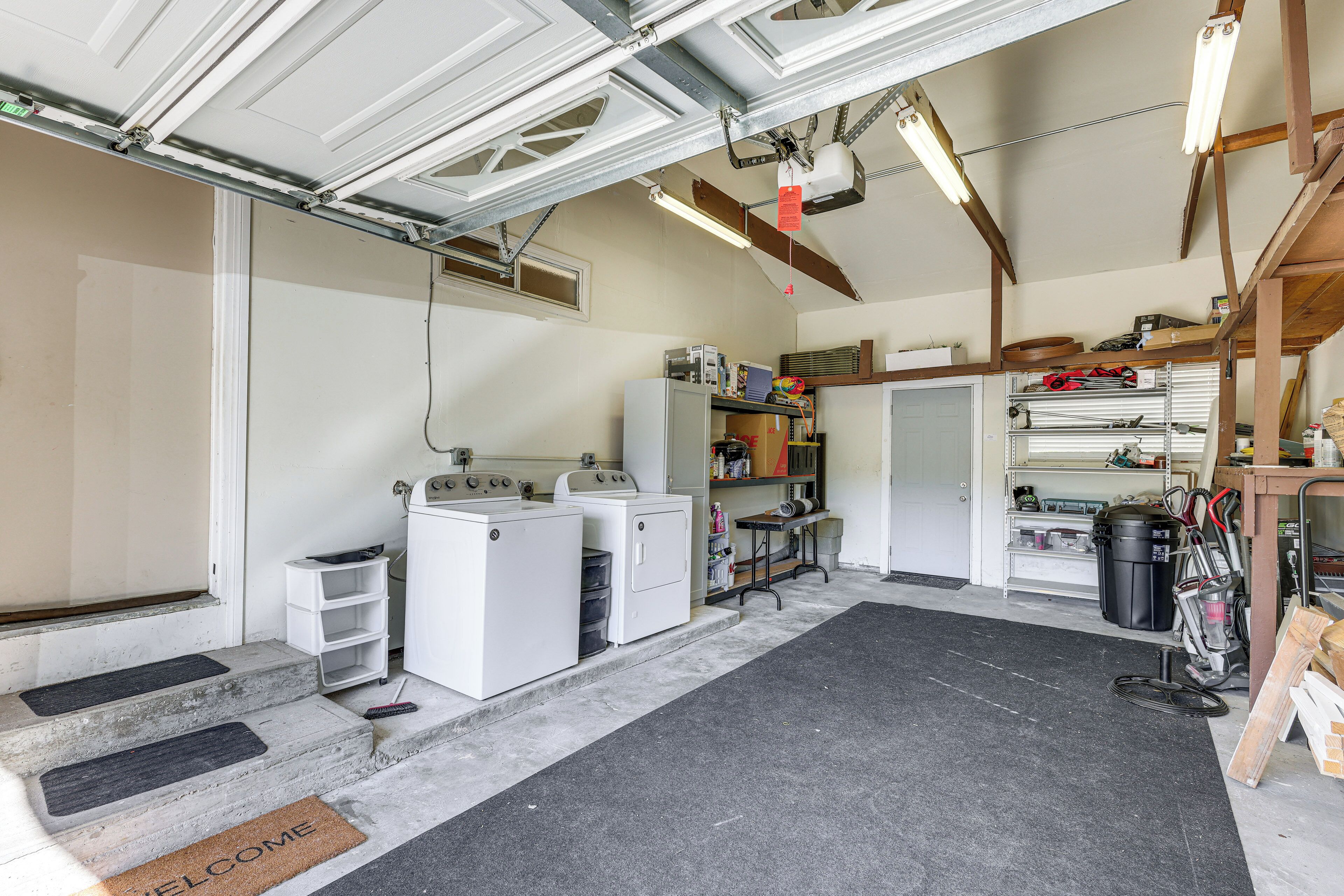 Un garage con lavatrice, scaffali attrezzi e un tappetino di benvenuto.