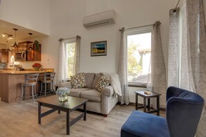 Un salon avec un canapé, une table basse et un fauteuil bleu. Il y a également un coin cuisine avec des placards en bois et un four à micro-ondes.