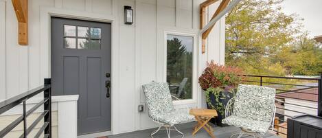 A wooden deck with two rocking chairs and a small table, a gray door, and a welcome mat.