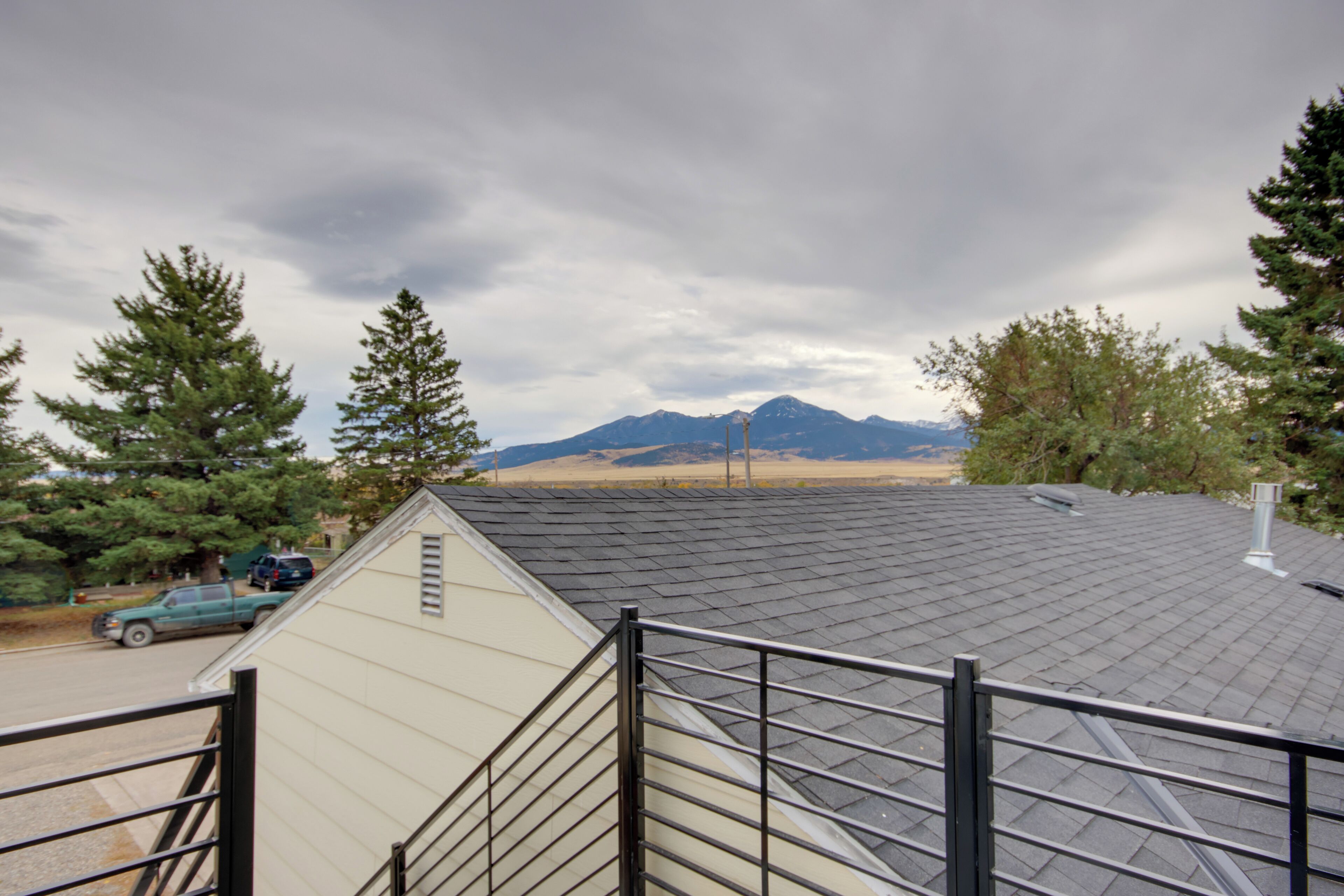 A view from a window overlooking a mountain range, a road with a parked vehicle, and a building with a sloped roof.