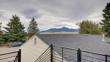 A view from a window overlooking a mountain range, a road with a parked vehicle, and a building with a sloped roof.
