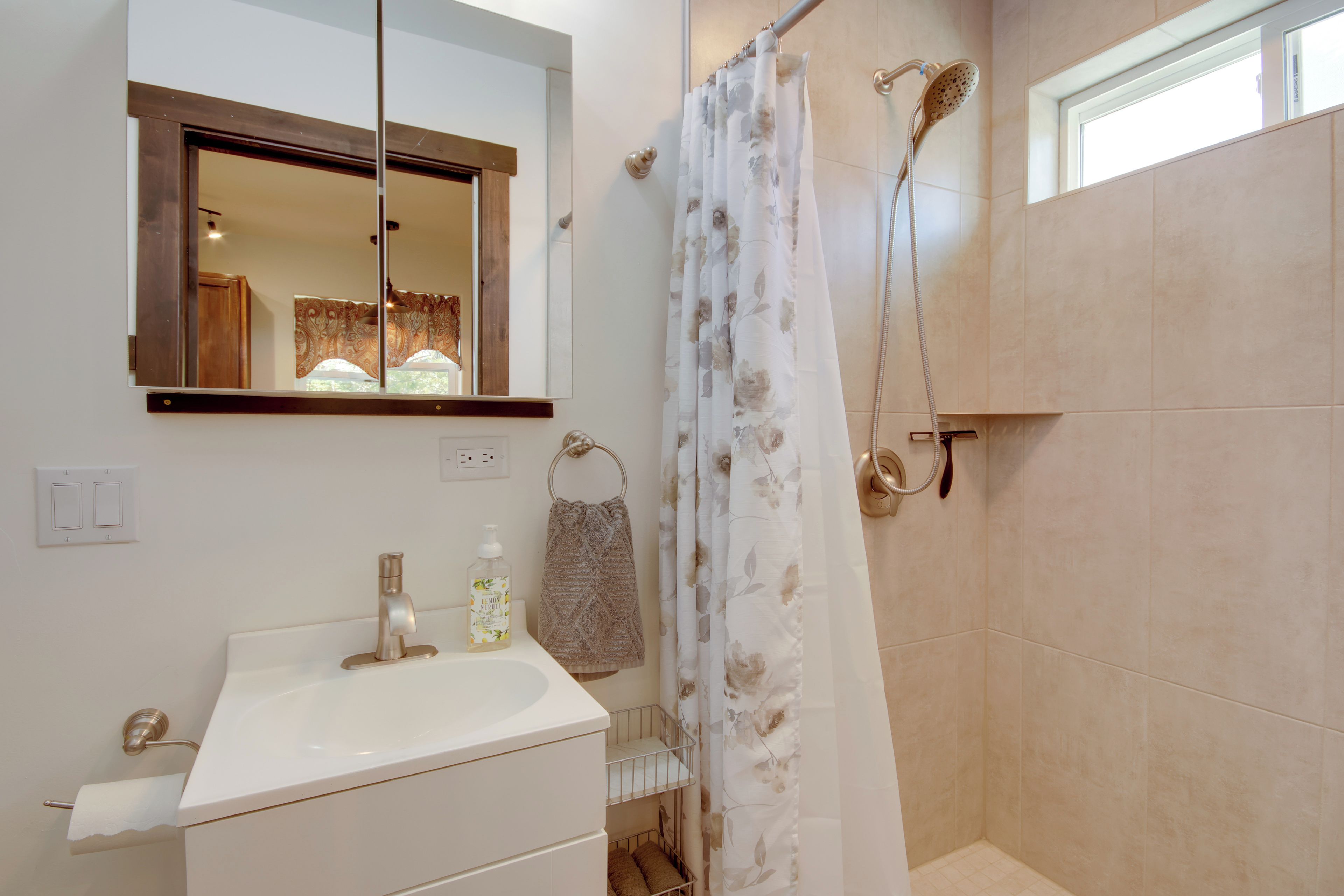 A bathroom with a white sink, a mirror, a shower with a floral curtain, and a towel rack.