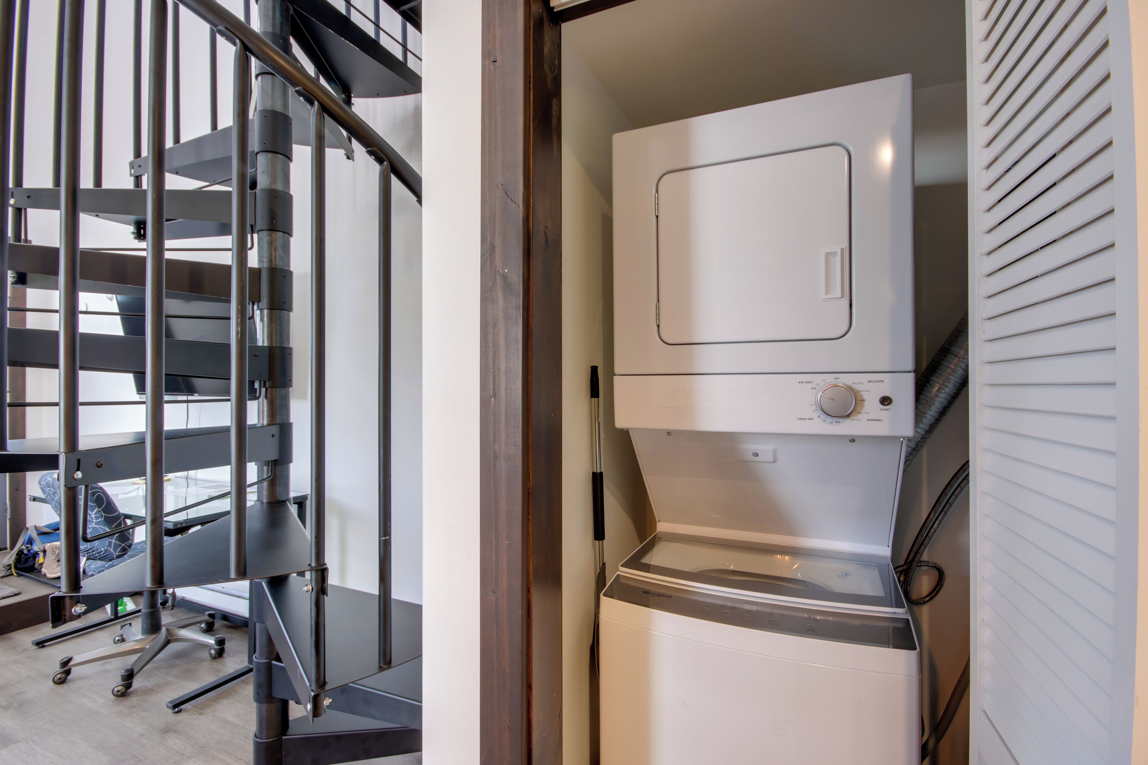A compact living space with a built-in washer and dryer, a metal staircase, and a small office area with a chair and desk.