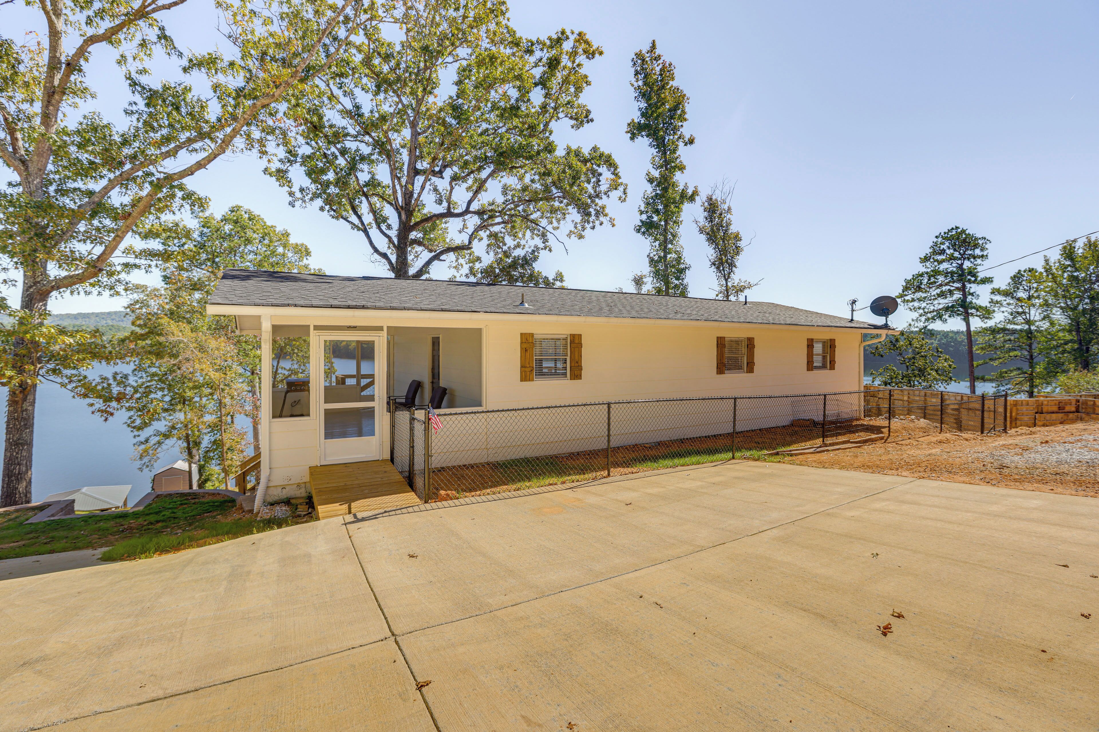 A single-story house with a covered porch, a fenced yard, and a view of a lake.