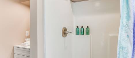 Ein Badezimmer mit einer weißen Duschkabine, einem weißen Schrank mit Schubladen und drei grünen Flaschen an der Wand.