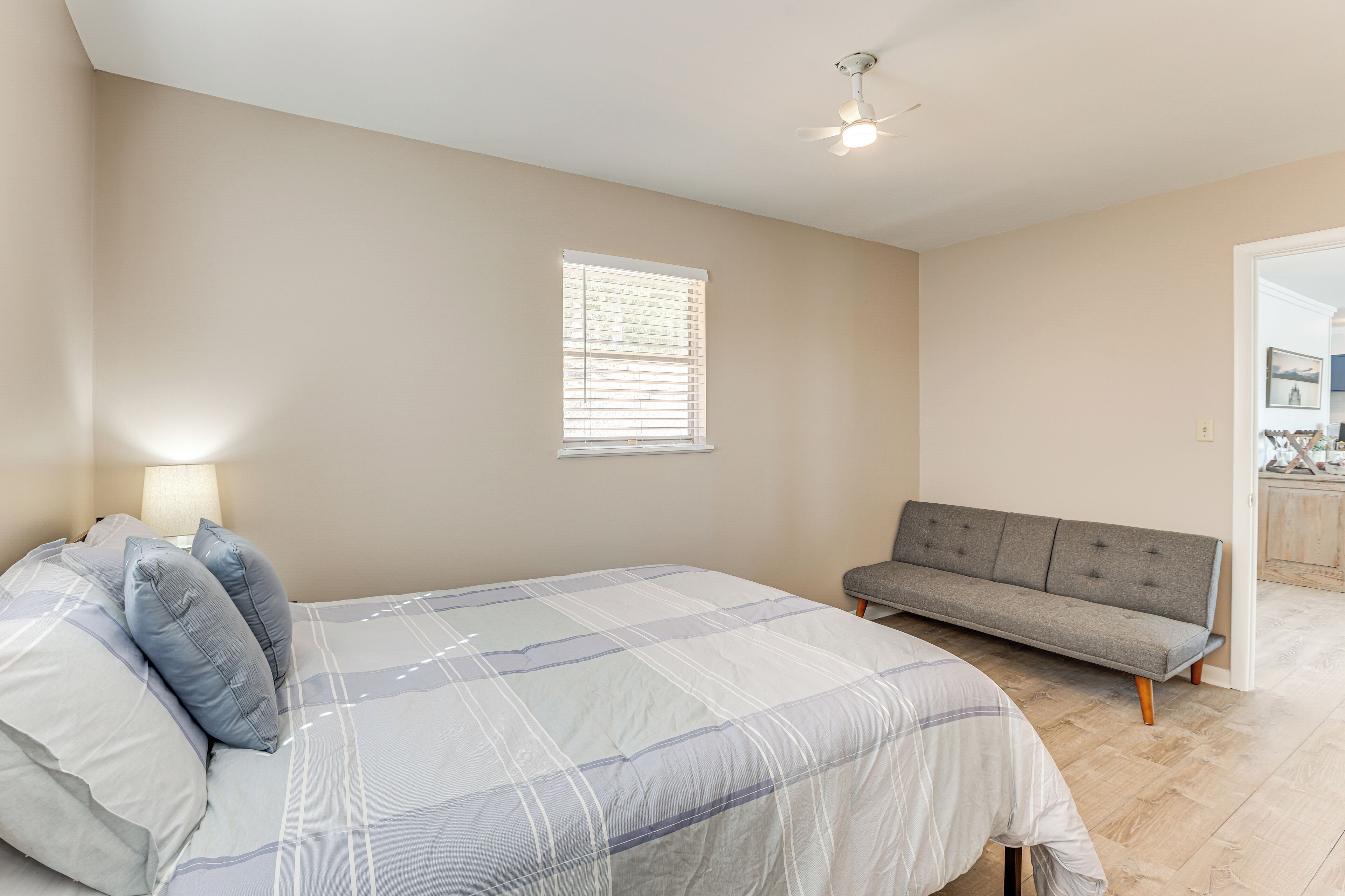 A bedroom with a bed, a grey sofa, a window with blinds, and a ceiling fan.