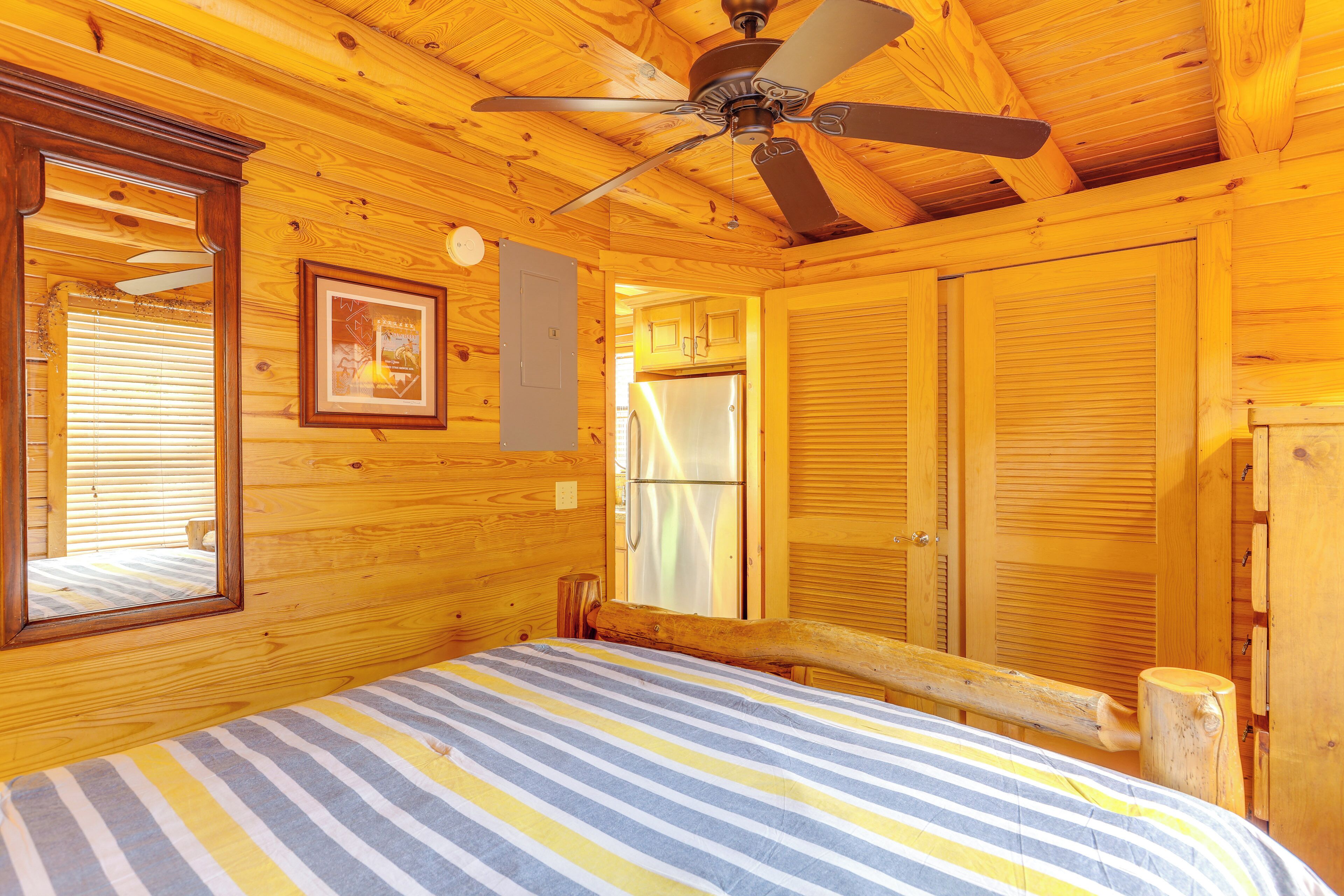A wooden cabin bedroom with a bed, a ceiling fan, a framed picture, and a window with blinds.