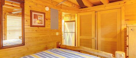 A wooden cabin bedroom with a bed, a ceiling fan, a framed picture, and a window with blinds.