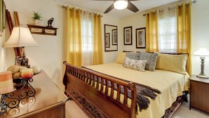 A bedroom with a wooden bed, yellow curtains, a ceiling fan, and framed pictures on the wall.