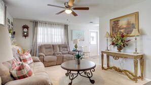A living room with a beige sofa, a round coffee table, a ceiling fan, and a decorative console table with a painting.