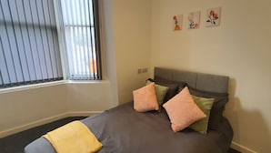 Una camera da letto con un letto, cuscini, una finestra con persiane e tre elementi decorativi a parete.