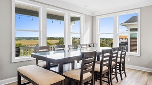 A dining area with a large table and chairs, large windows with a view of the countryside, and a ceiling fan. - Carolina Kai, 7 Bedroom, Second Row w/ Private pool & Elevator (Ocean Isle Beach)