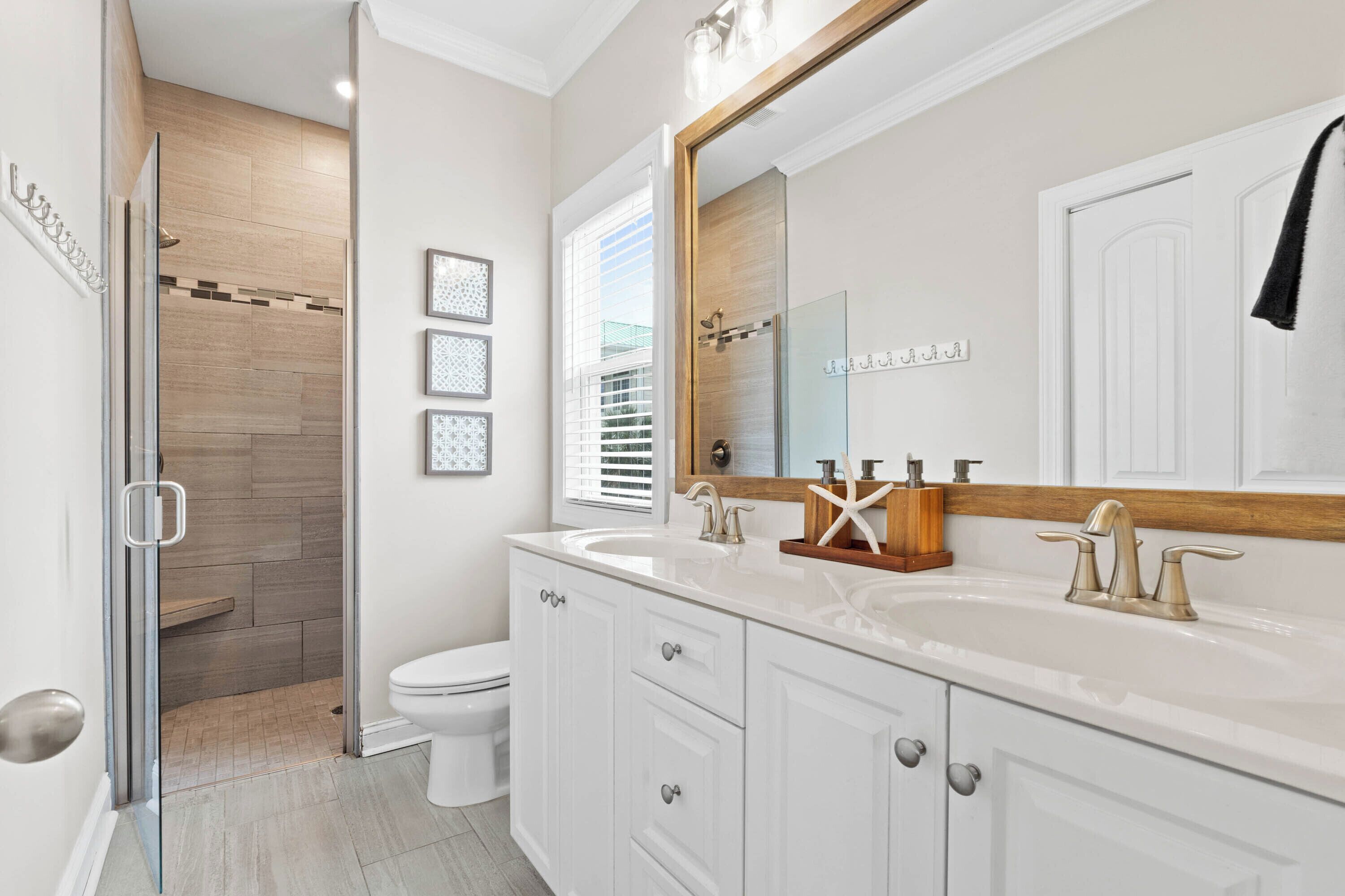 A modern bathroom with a glass shower enclosure, a white toilet, a vanity with a large mirror, and a sink with two faucets.