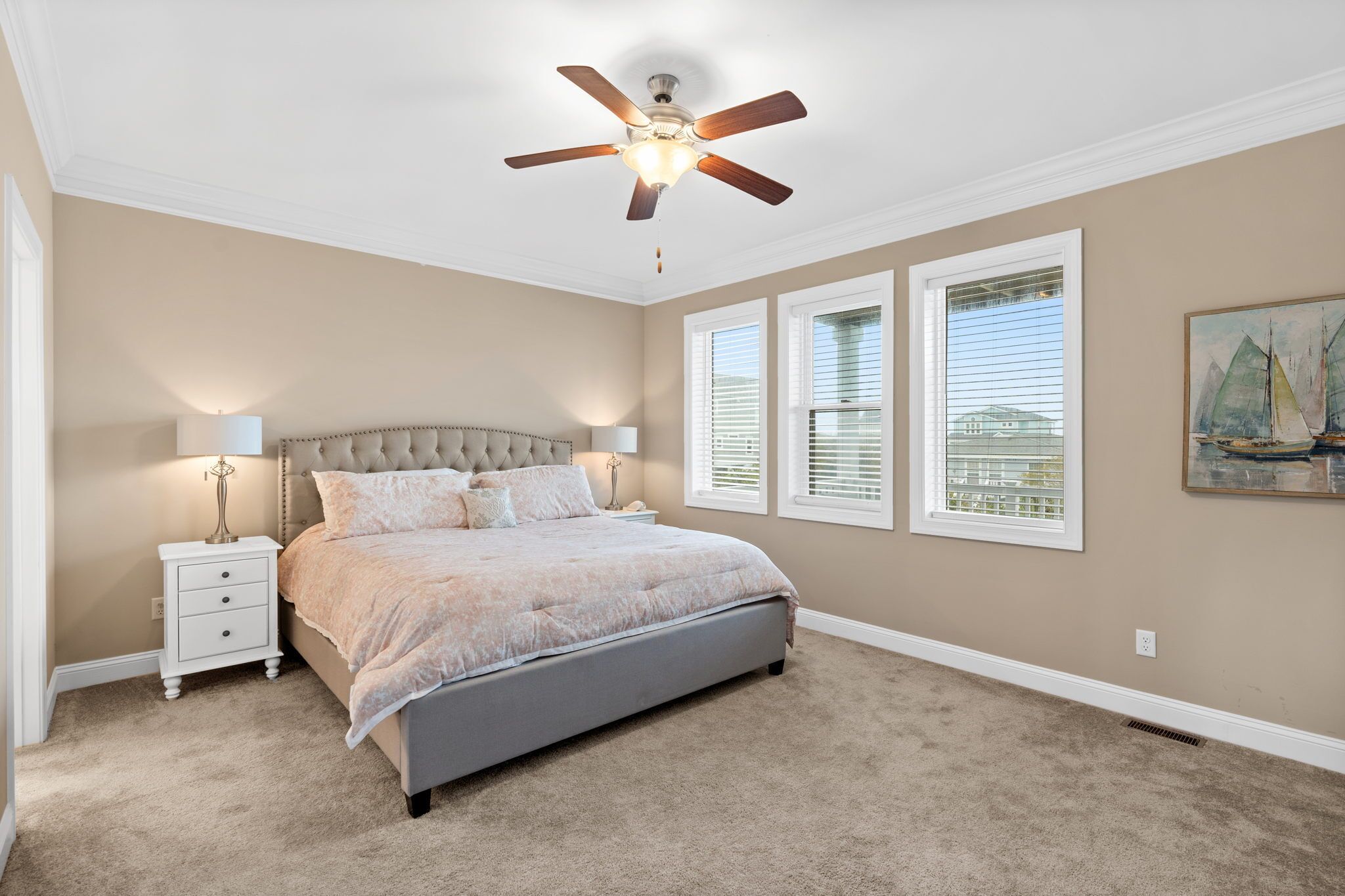 A bedroom with a bed, nightstands, a ceiling fan, and windows.
