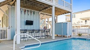 A pool area with a bar and chairs, a TV mounted on the wall, and a white fence surrounding the pool. - Easy Breezy is a 4 bedroom, 5 bathroom house w/ private pool & elevator (Sunset Beach)