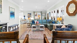 A spacious living room with a large sofa, a coffee table, and a dining area with a kitchen in the background. - Easy Breezy is a 4 bedroom, 5 bathroom house w/ private pool & elevator (Sunset Beach)