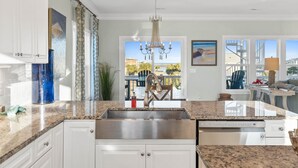 A modern kitchen with granite countertops, stainless steel appliances, and a large window offering a view of the outdoors. - Easy Breezy is a 4 bedroom, 5 bathroom house w/ private pool & elevator (Sunset Beach)