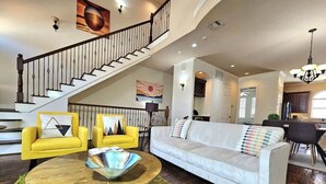 A spacious living room with a staircase, yellow armchairs, a white sofa, and a round coffee table.