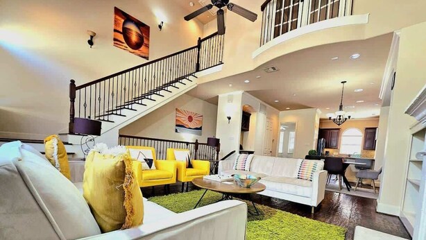 A spacious living area with a staircase, a white sofa, yellow chairs, and a green rug.