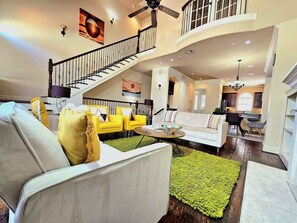 Un amplio espacio habitable con una escalera, un sofá blanco, sillas amarillas y una alfombra verde.