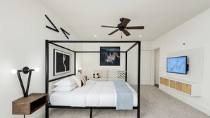 A modern bedroom with a four-poster bed, a ceiling fan, a mounted TV, and artwork on the walls.