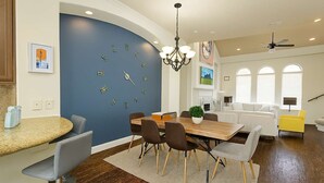 A modern kitchen with a curved blue accent wall, a dining area with a wooden table and chairs, and a bright yellow armchair.
