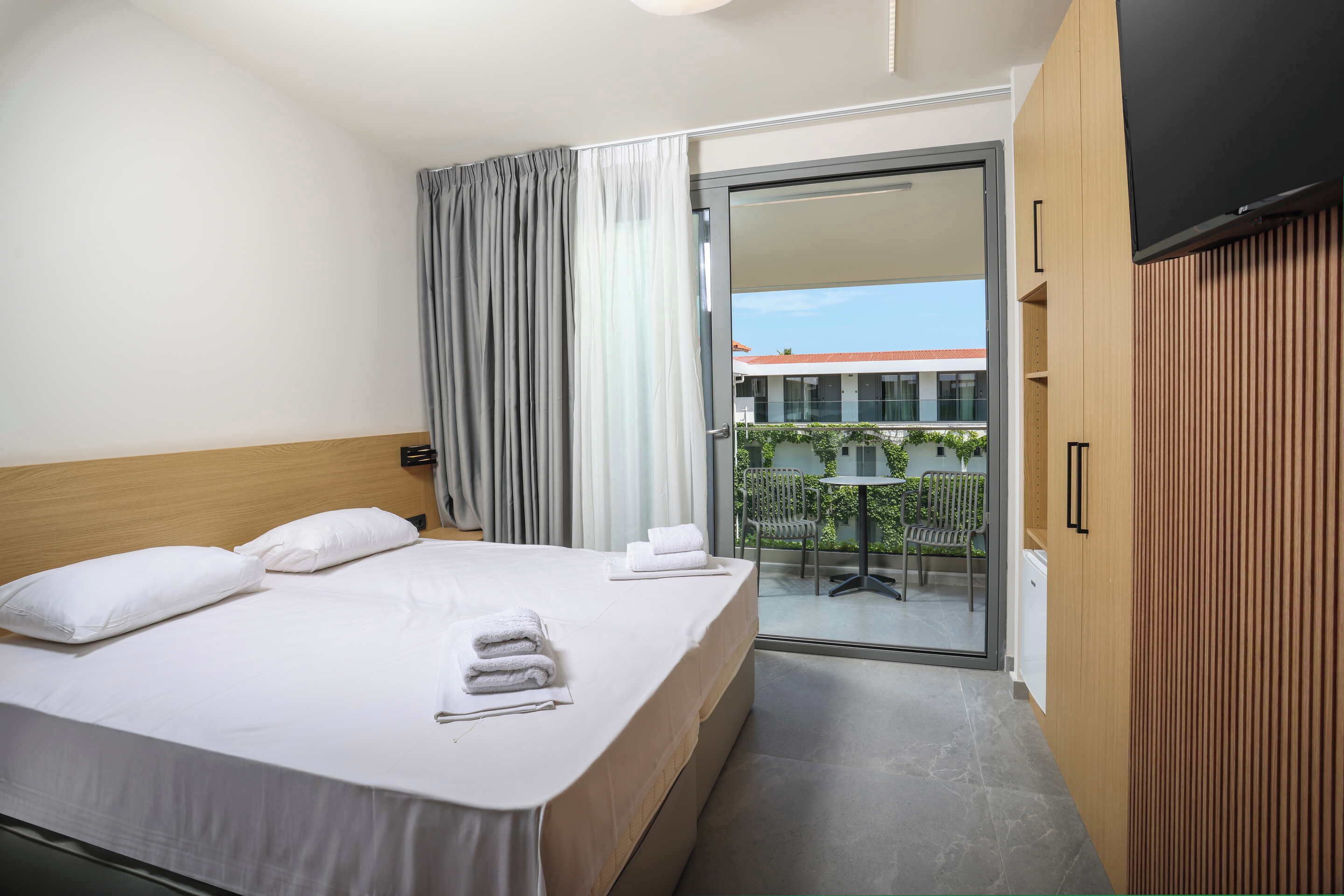 Een hotelkamer met een bed, een televisie, een schuifglasdeur naar een balkon en een houten garderobe.