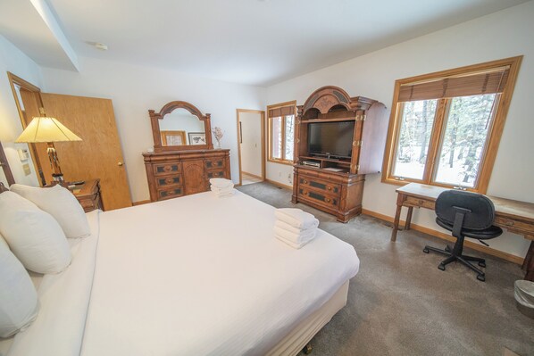 A hotel room with a large bed, wooden dresser, television, desk, and a window with blinds.