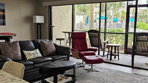 Una sala de estar moderna con un sofá de cuero, un sillón rojo y una mesa de centro. Una ventana grande ofrece vistas al exterior.