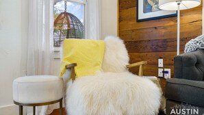 A cozy room with a wooden wall, a white chair, a fluffy white sofa, and a grey couch.