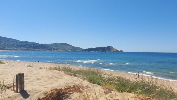 A beach with clear blue water, sandy shore, and a hill in the background. - 123 Sun and Relaxation (Tabarka)