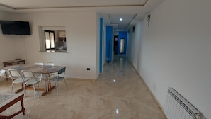A spacious living area with a dining table and chairs, a TV mounted on the wall, and a kitchen visible through an open doorway. - 123 Sun and Relaxation (Tabarka)