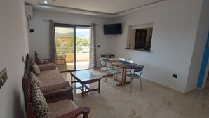 A living room with a sofa set, a dining table with chairs, a TV mounted on the wall, and a balcony with a view of the outside. - 123 Sun and Relaxation (Tabarka)