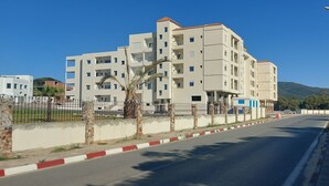 A multi-story residential building with balconies, a paved road with a red and white curb, and a clear blue sky. - 123 Sun and Relaxation (Tabarka)