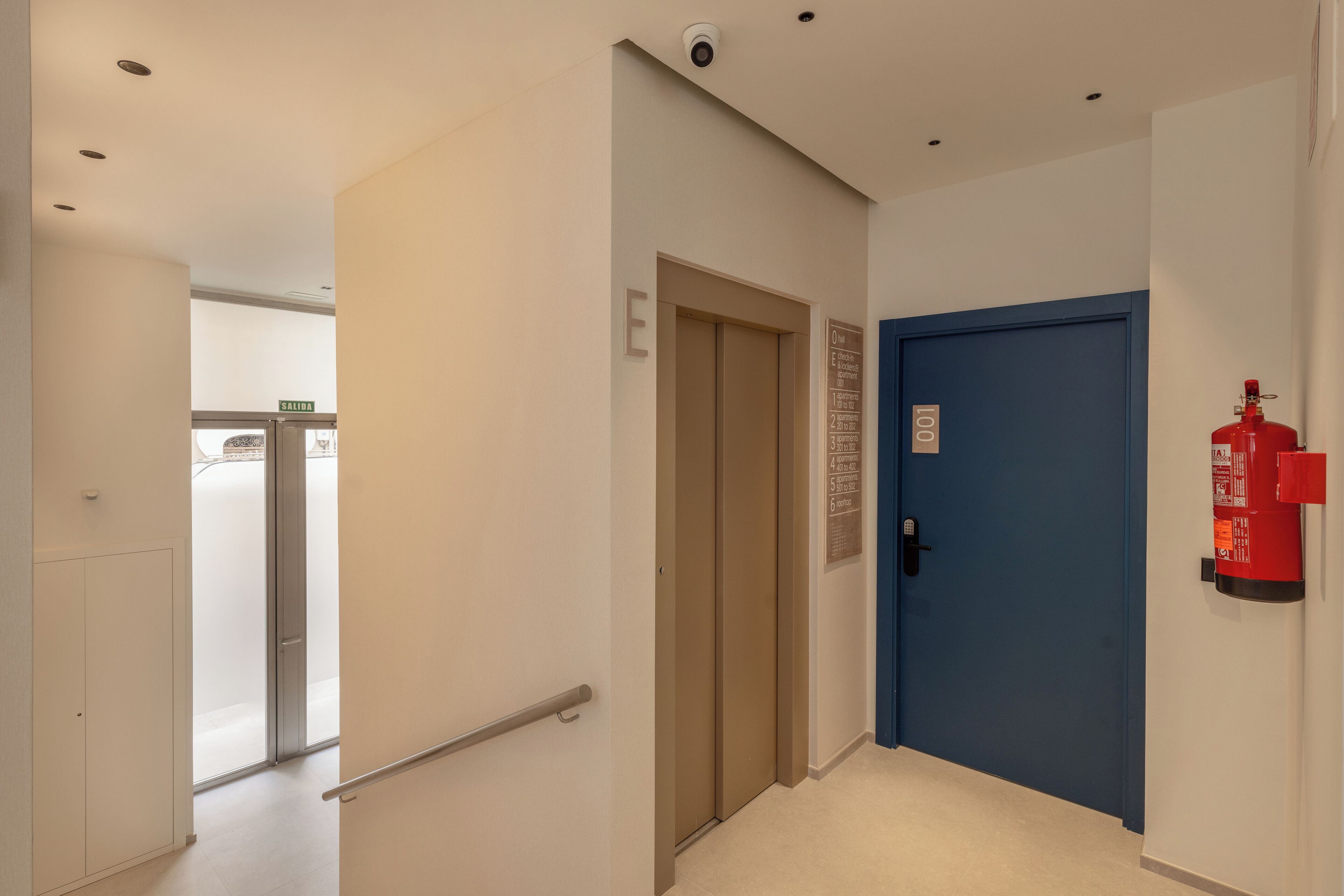 A hallway with a blue door, a fire extinguisher, and an elevator.