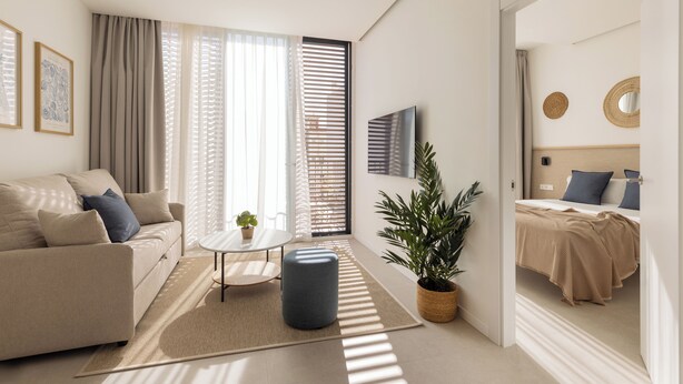 Ein modernes, helles Wohnzimmer mit einer Couch, einem Couchtisch und einer Topfpflanze.