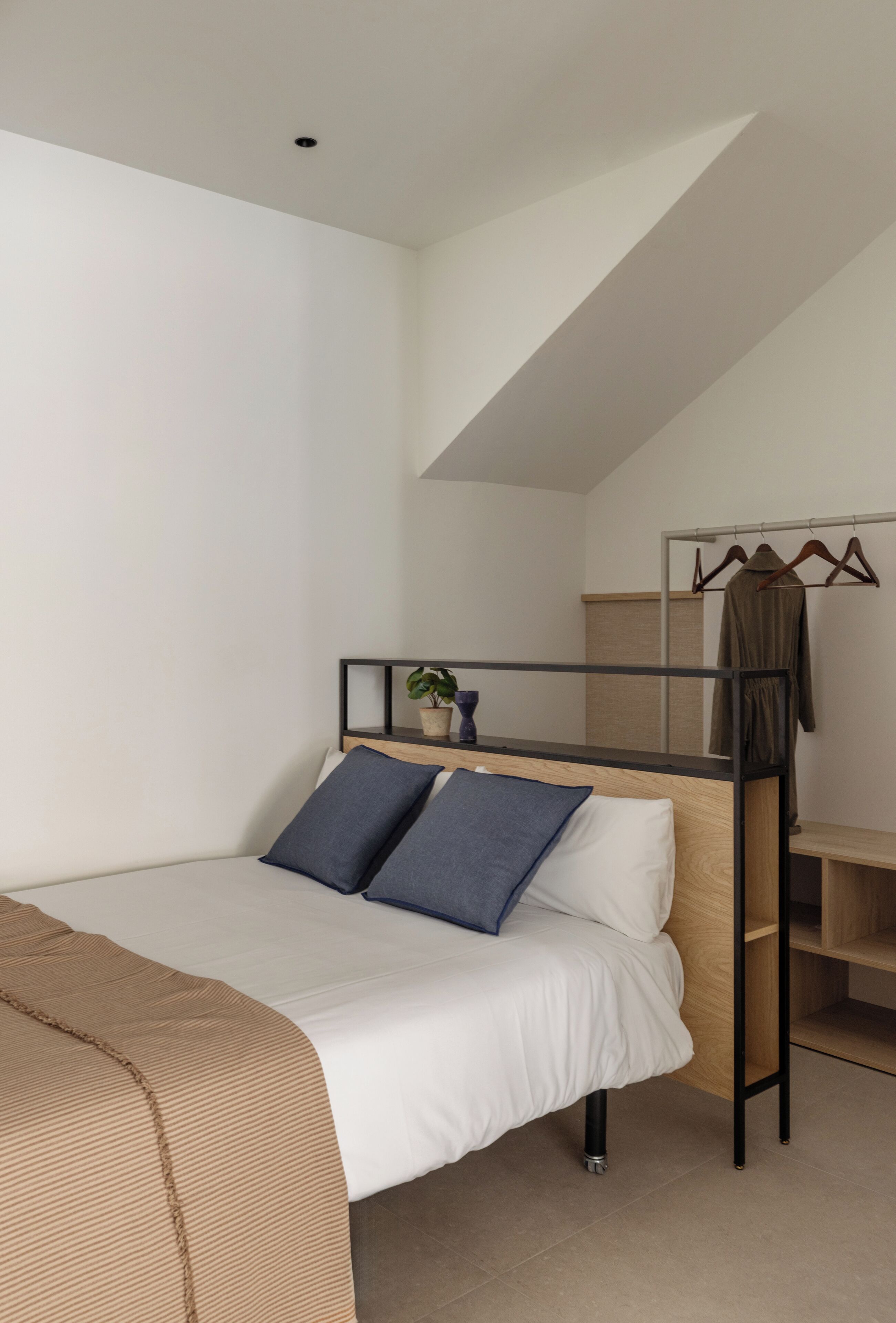 Une chambre moderne et compacte, équipée d’un lit superposé, d’un petit bureau, d’un porte-vêtements et d’une plante en pot.