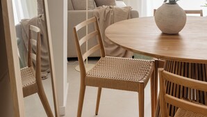 Ein Essbereich mit einem runden Holztisch, zwei Korbstühlen, einem großen Spiegel und einer Pendelleuchte.