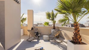 Eine Dachterrasse mit zwei Liegestühlen, einem kleinen Tisch mit einer Zeitschrift und einem Blumentopf.